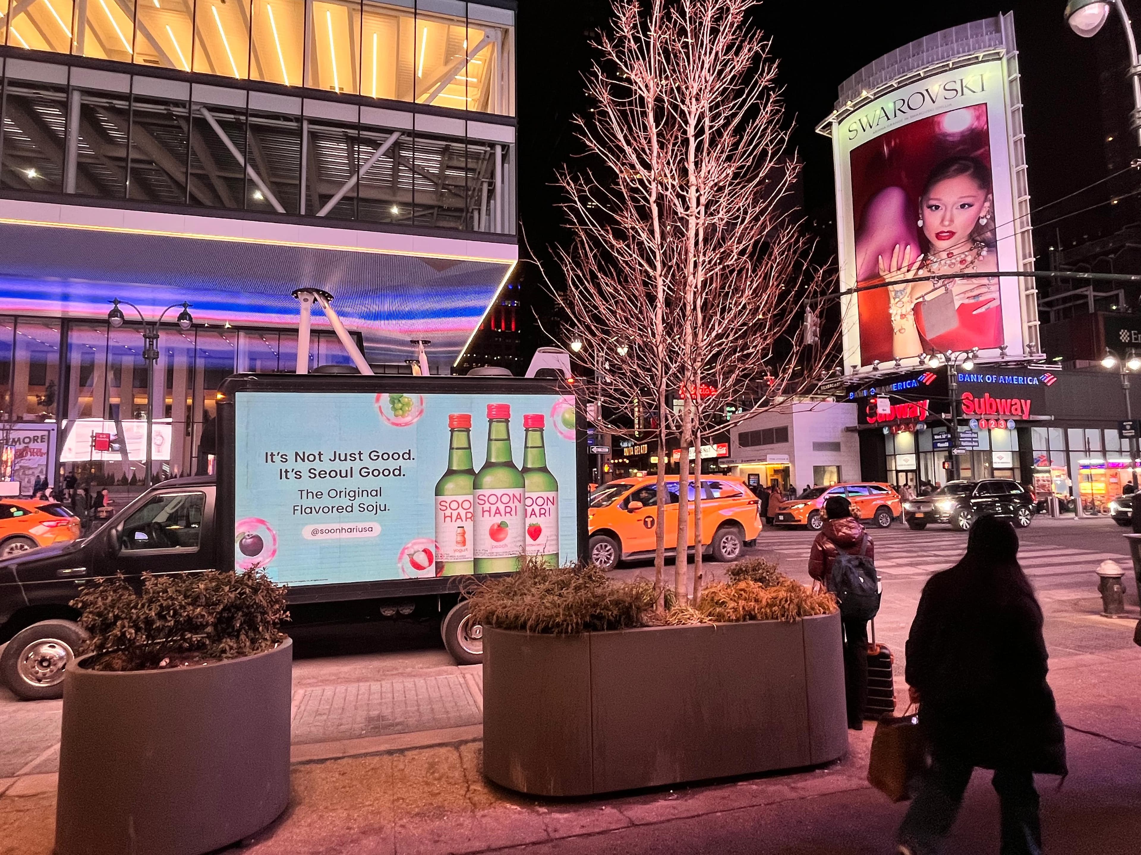 Busy city street at night with a soju advertisement truck and large Swarovski billboard.